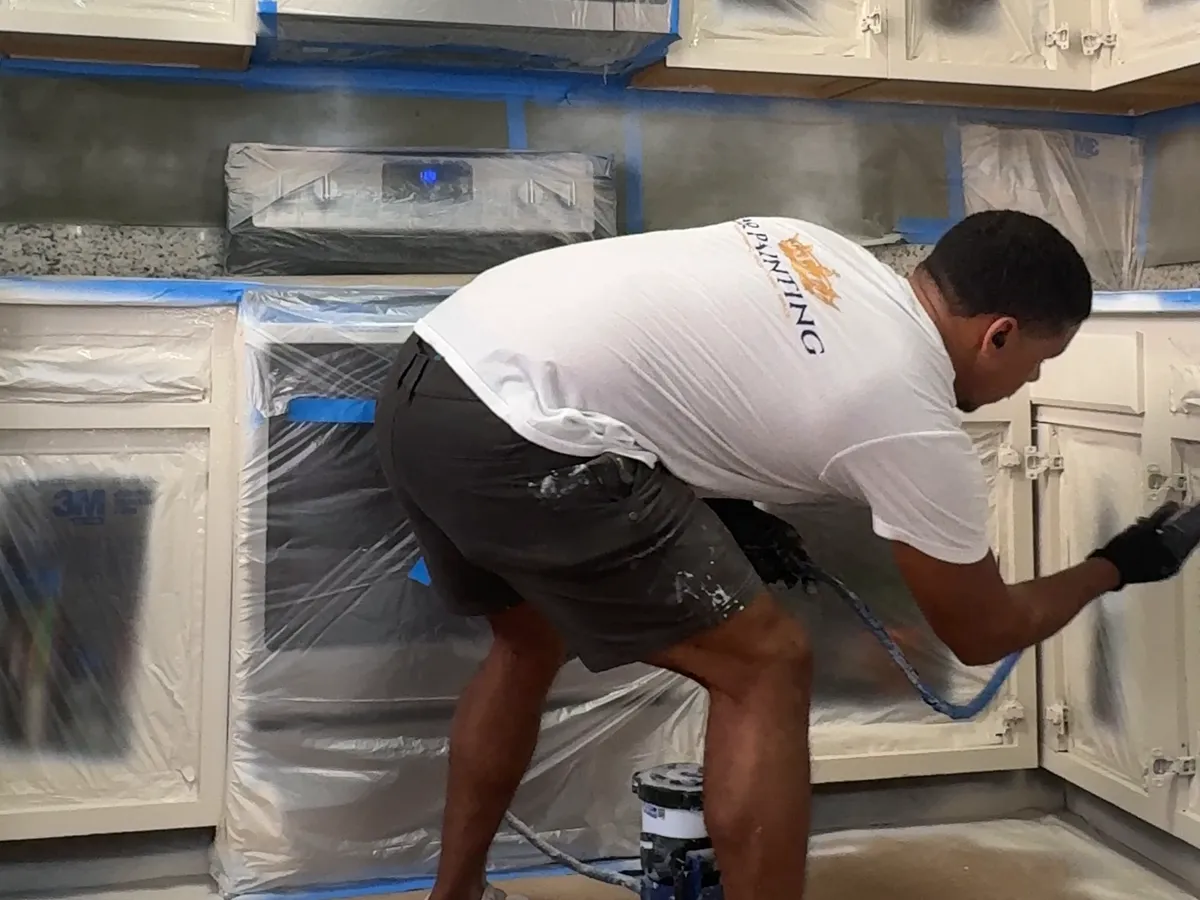 Leandro spraying the lower cabinets in a fully covered kitchen, seen from the side