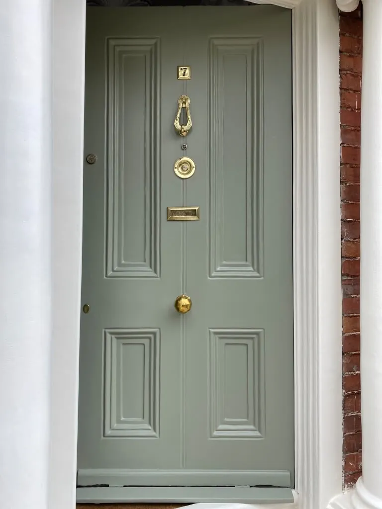 Front door painted soft grey-green with a brass knocker and white trim