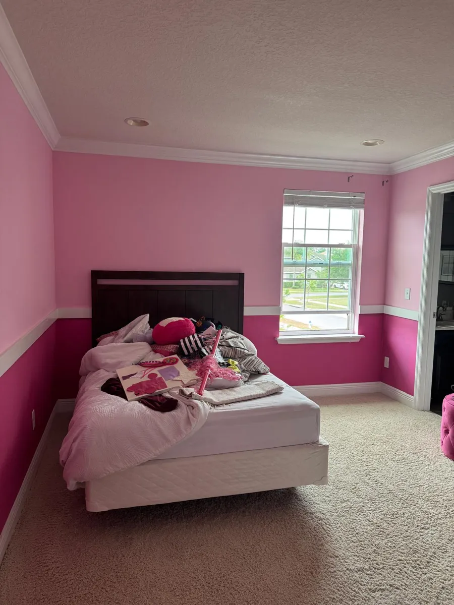Finished bedroom in soft pink above a white chair rail and deep magenta below, with the bed by the window